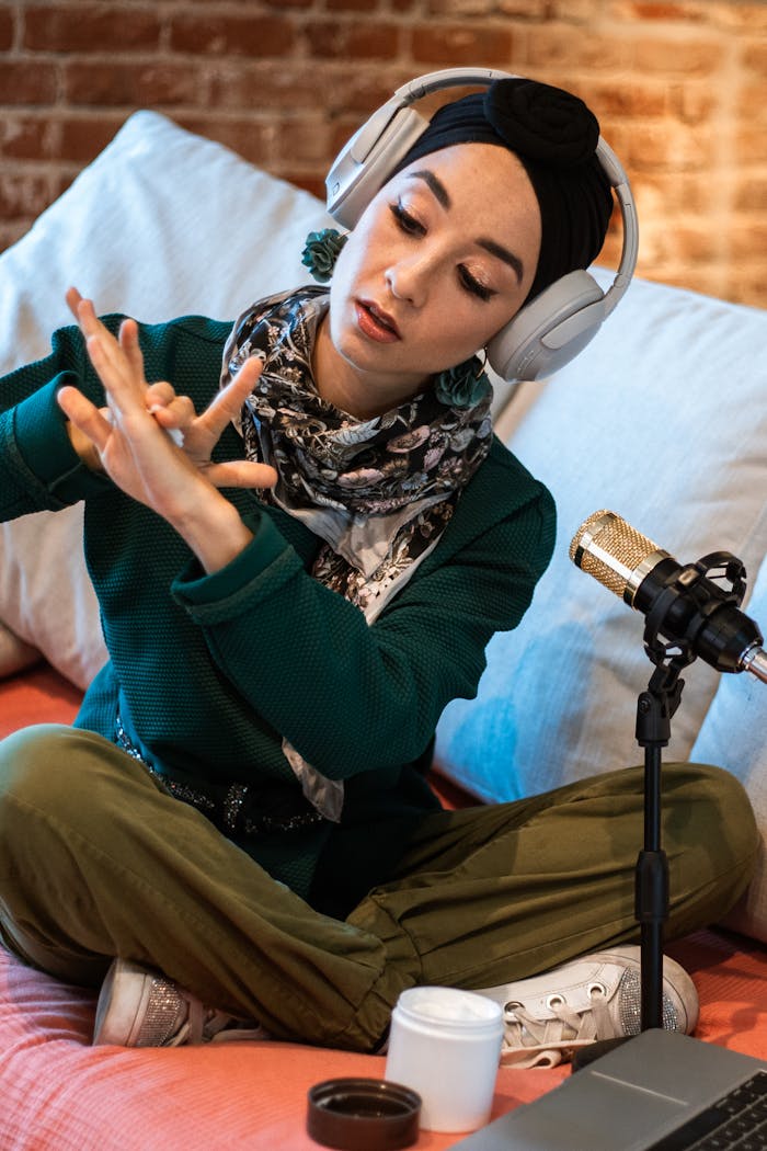 Young woman wearing headphones, podcasting with a condenser microphone in a cozy setting.